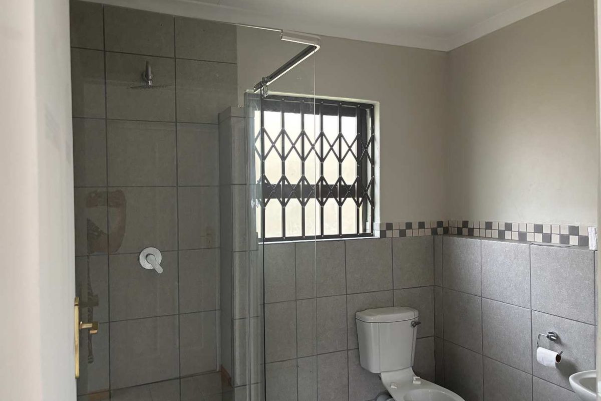 A clean and functional bathroom featuring a walk-in shower with glass screen, tiled walls, and a security gate on the window.