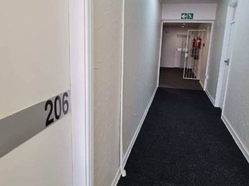 A clean, functional office building hallway featuring dark carpeting, white walls, and standard office door access.