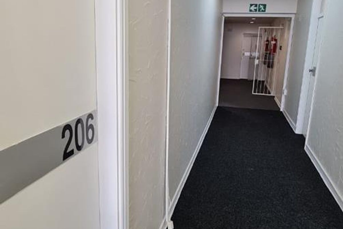 A clean, functional office building hallway featuring dark carpeting, white walls, and standard office door access.