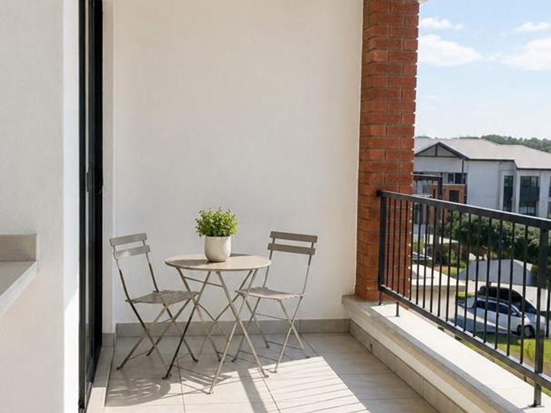 A well-maintained covered balcony featuring tiled flooring, a brick support pillar, and a metal balustrade with views of the surrounding residential area.