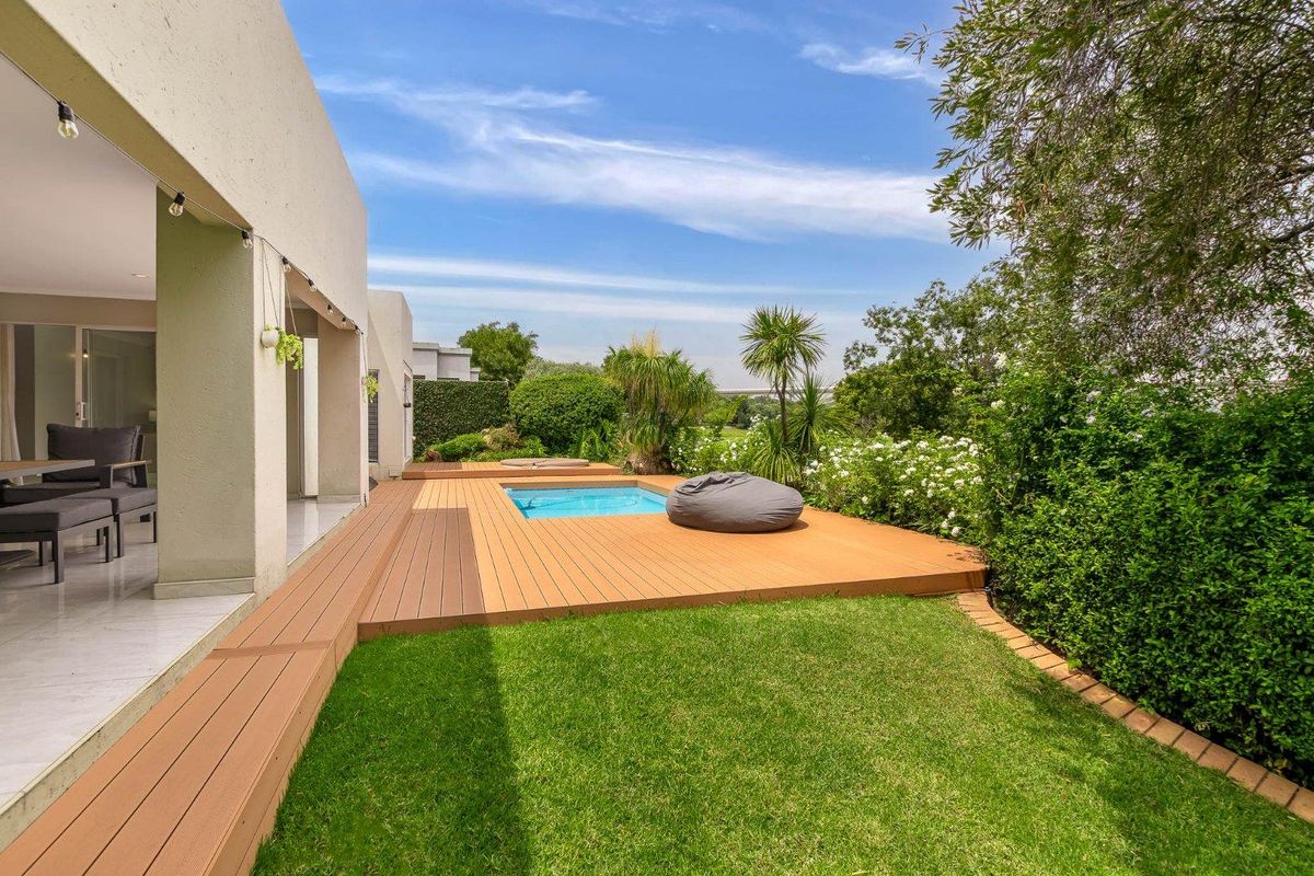 A well-maintained rear garden featuring a composite timber deck, a built-in swimming pool, and a manicured lawn area.