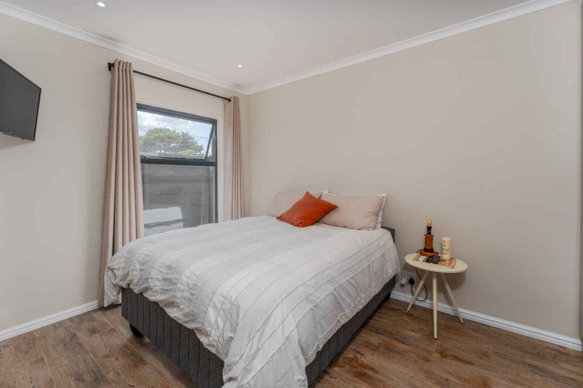 A well-maintained bedroom featuring neutral wall tones, wood-look flooring, and a large window with curtain tracks.