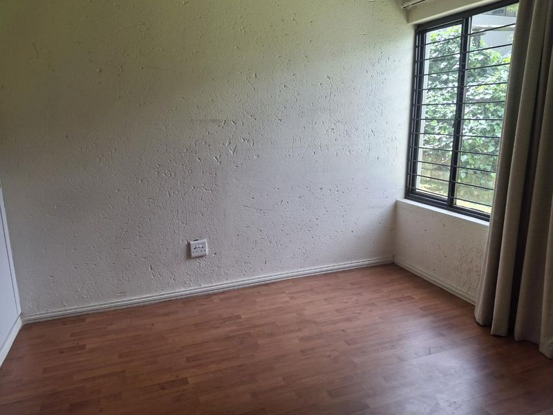 An empty bedroom featuring laminate flooring, textured walls, and a window fitted with security bars.