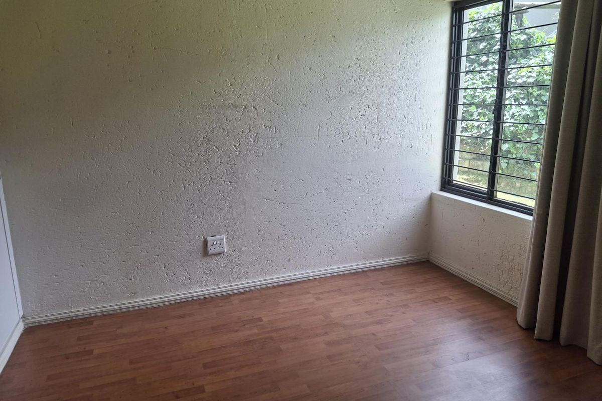 An empty bedroom featuring laminate flooring, textured walls, and a window fitted with security bars.
