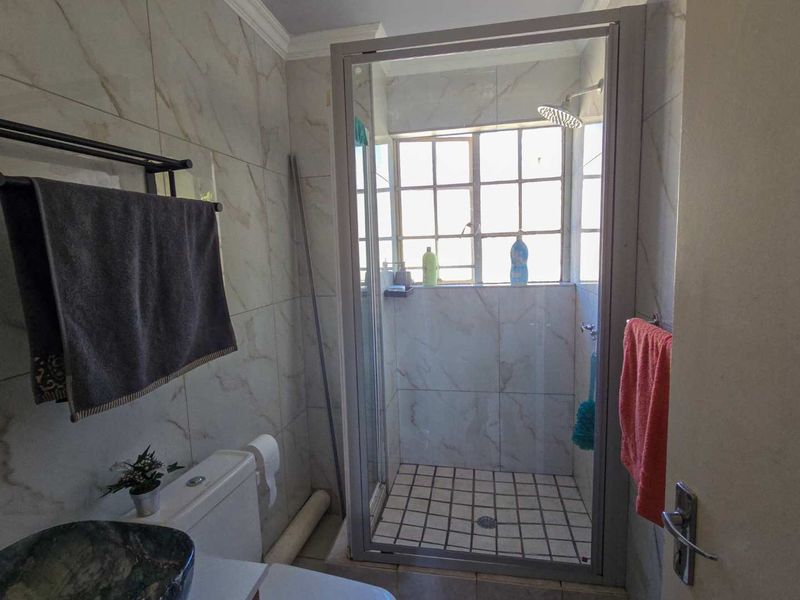 A functional bathroom featuring a tiled shower enclosure, toilet, and marble-effect wall tiling with natural light from a window.