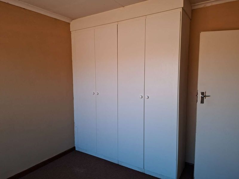 A vacant bedroom featuring a large built-in wardrobe, carpeted flooring, and neutral wall finishes, offering a blank canvas for potential updates.
