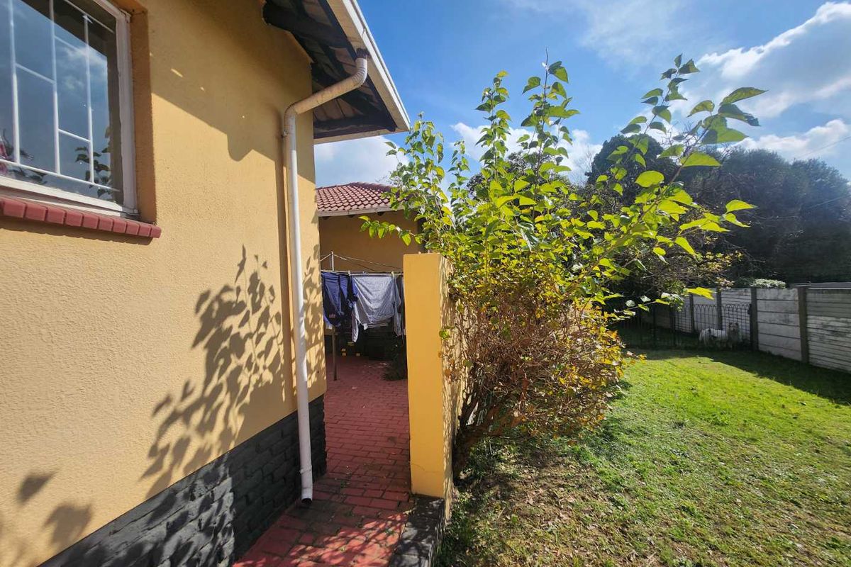 A view of the side exterior of the house featuring a paved walkway, yellow plastered walls, and a small garden area with boundary fencing.