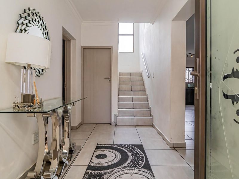 A bright and welcoming entrance hall featuring tiled flooring and a staircase with a metal handrail, leading to the upper level of the home.