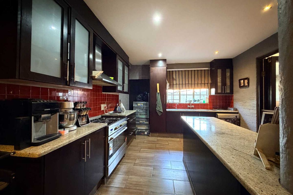 A spacious kitchen featuring dark cabinetry, granite countertops, a central island, gas stove, and a vibrant red tiled backsplash.
