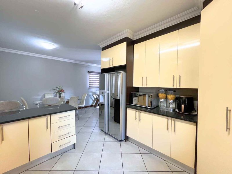 Open-plan kitchen and dining area featuring cream-toned built-in cabinetry, dark granite countertops, and neutral tiled flooring throughout.