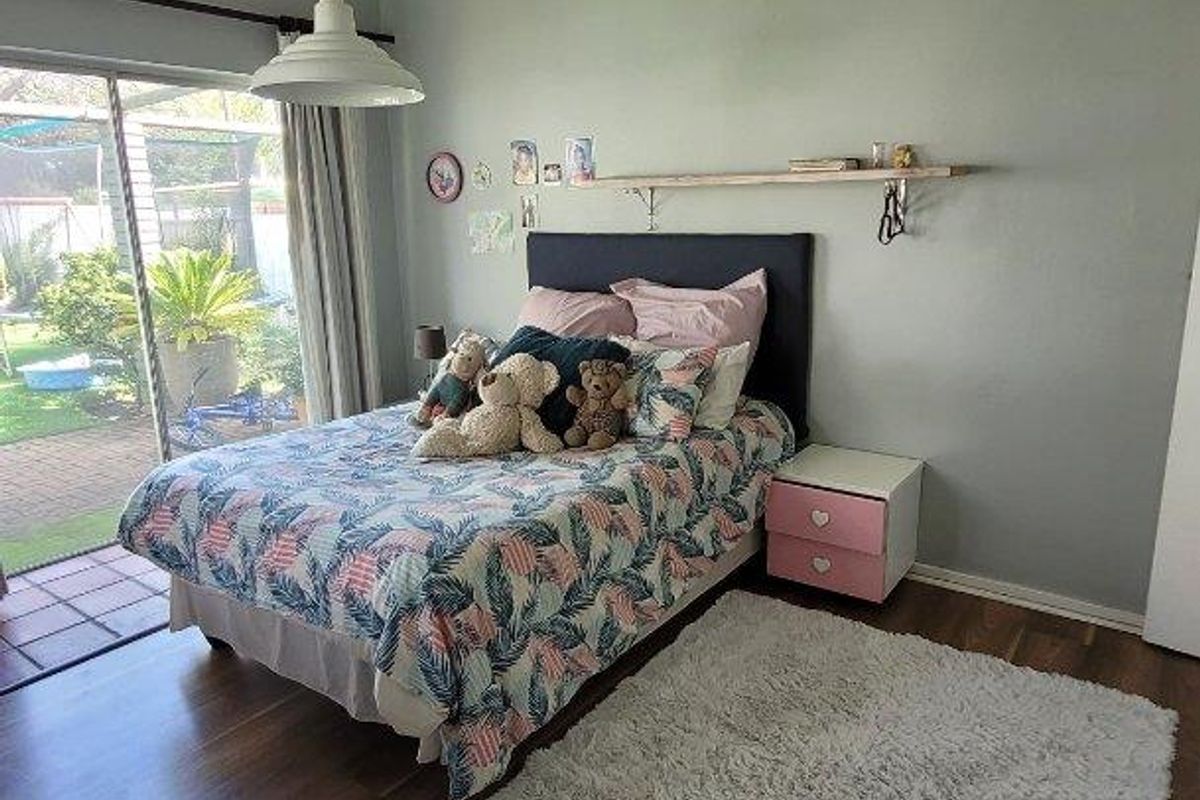 A bright bedroom featuring wood-look flooring, a pendant light fixture, and sliding glass doors providing direct access to the rear patio and garden.