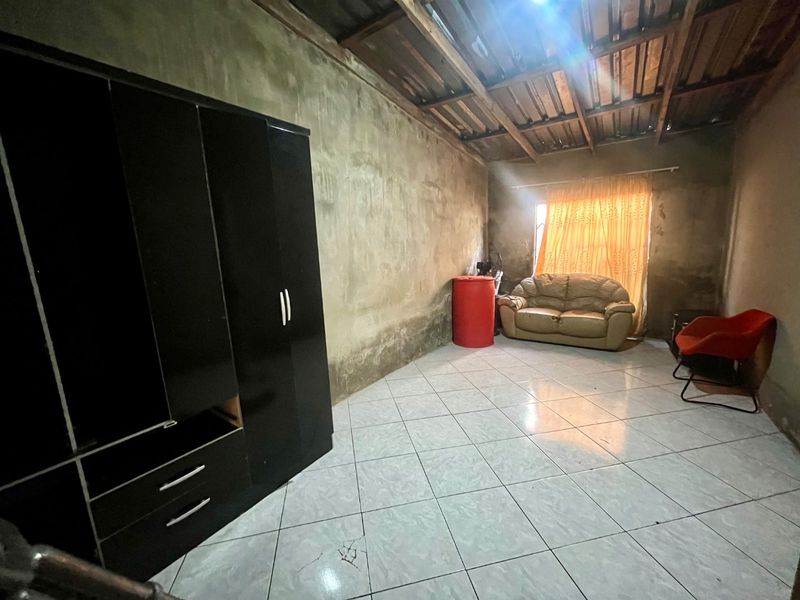 A living area featuring tiled flooring and exposed timber ceiling beams, currently requiring significant wall finishing and cosmetic updates.
