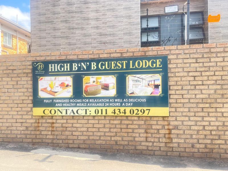 Front exterior view of the guest lodge featuring a brick boundary wall with integrated signage and electric security fencing.