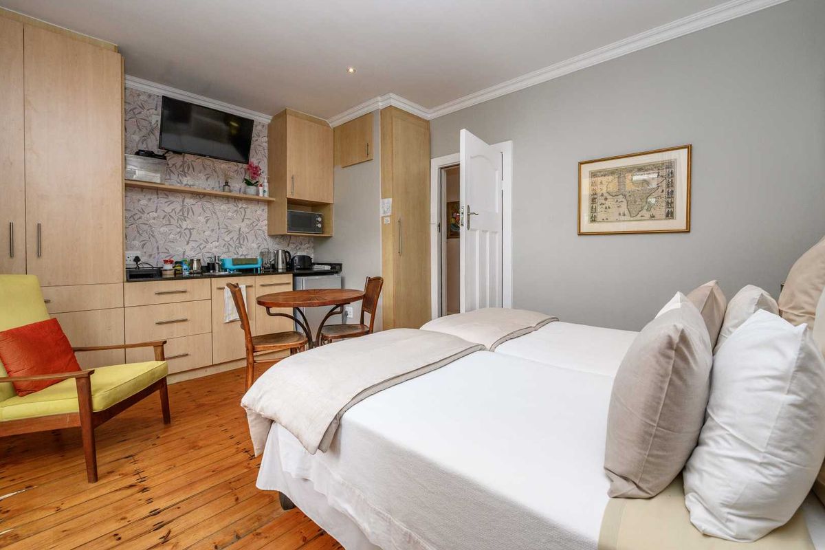 A bedroom featuring polished timber flooring, built-in cabinetry with integrated kitchenette facilities, and crown molding.