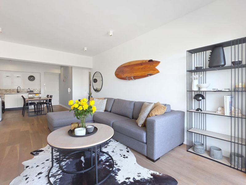 A bright open-plan living and dining area featuring light timber flooring, recessed lighting, and a modern kitchen with a tiled backsplash.