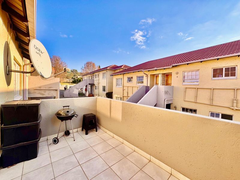 An open-air balcony featuring tiled flooring and a parapet wall, overlooking the apartment complex grounds.