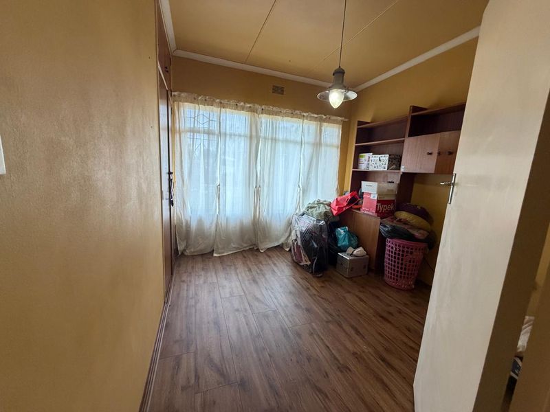 A bedroom featuring laminate flooring, a built-in cupboard, and a window with a security gate, offering a functional space for rest or storage.