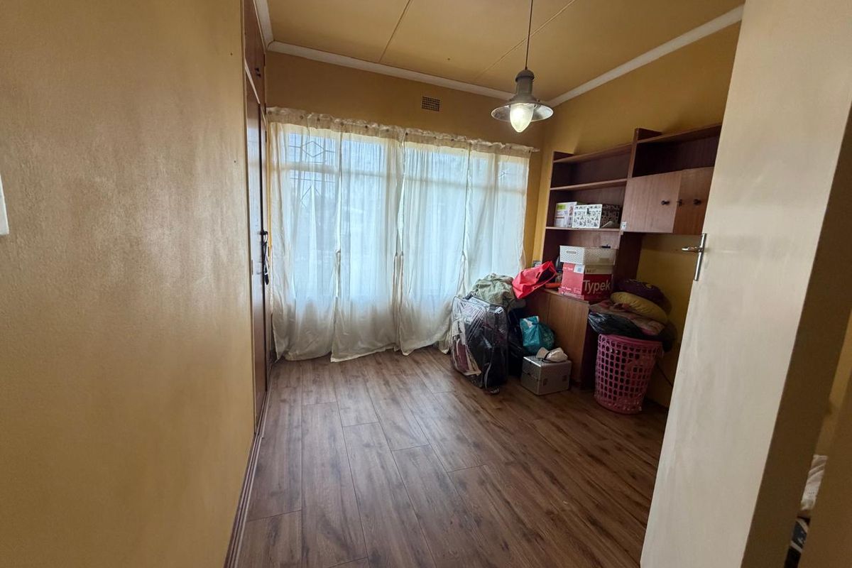 A bedroom featuring laminate flooring, a built-in cupboard, and a window with a security gate, offering a functional space for rest or storage.
