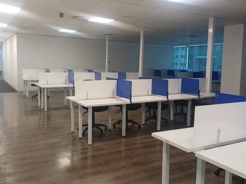 Open-plan office space featuring laminate flooring, suspended ceilings with recessed lighting, and large windows providing natural light.