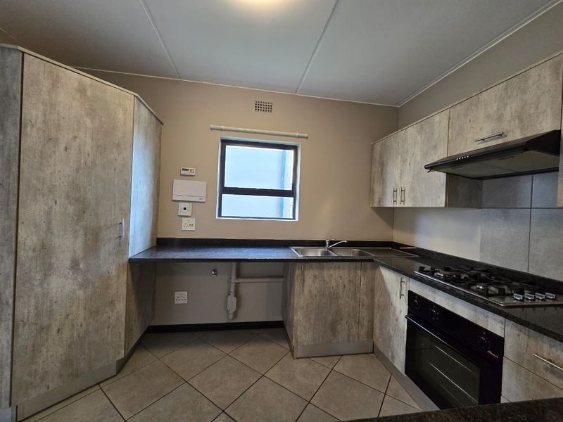 A functional kitchen featuring modern textured cabinetry, dark countertops, a gas hob, built-in oven, and tiled flooring.
