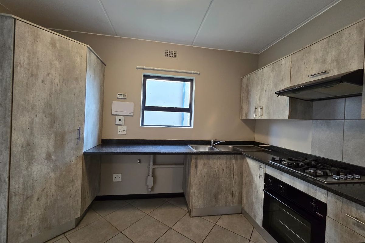 A functional kitchen featuring modern textured cabinetry, dark countertops, a gas hob, built-in oven, and tiled flooring.