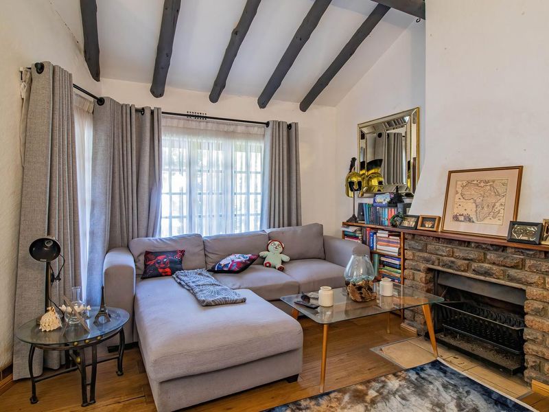 Cozy living room featuring exposed timber ceiling beams, a traditional brick fireplace, and timber flooring, creating a warm and inviting atmosphere.