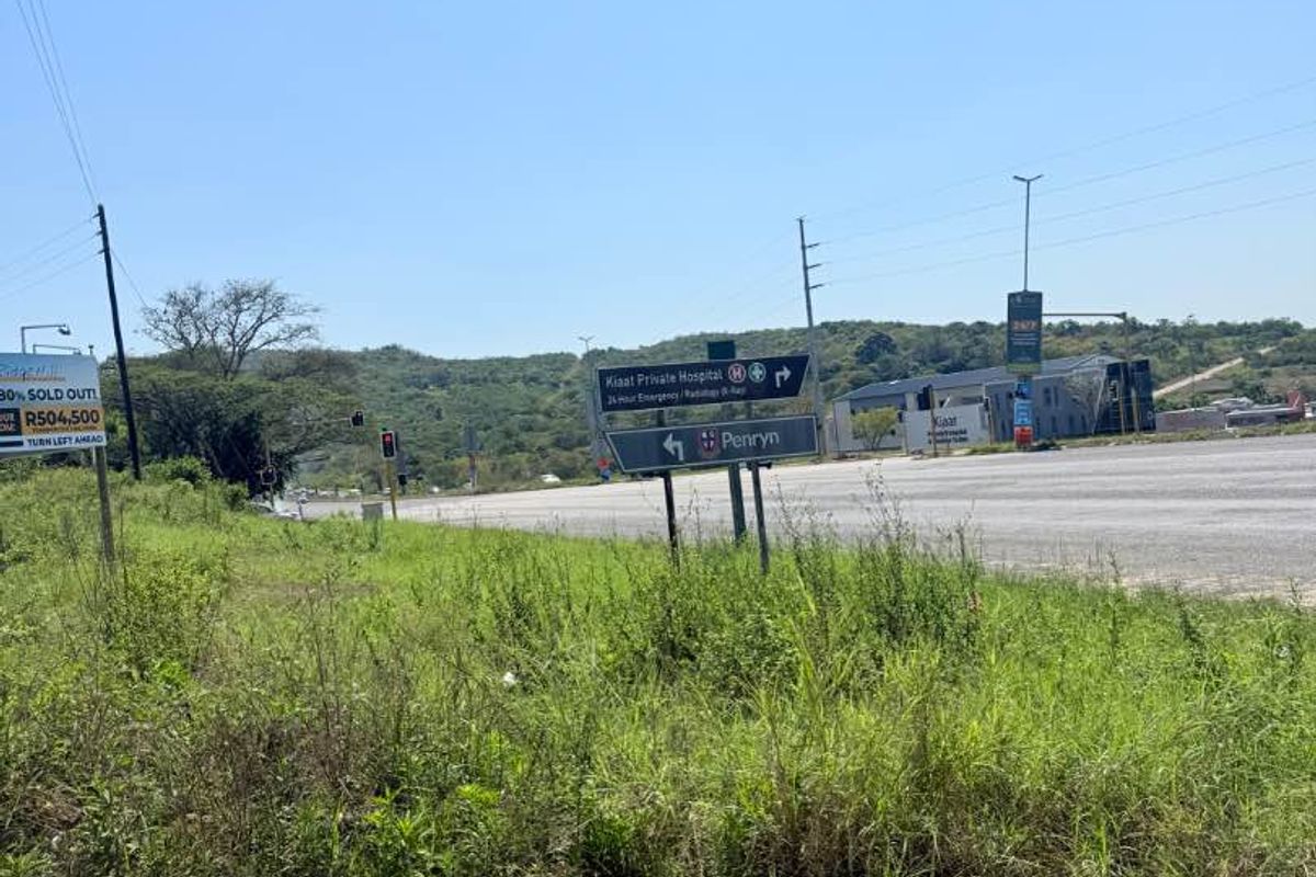 A street-level view of the vacant land showing proximity to local infrastructure, main roads, and nearby signage.