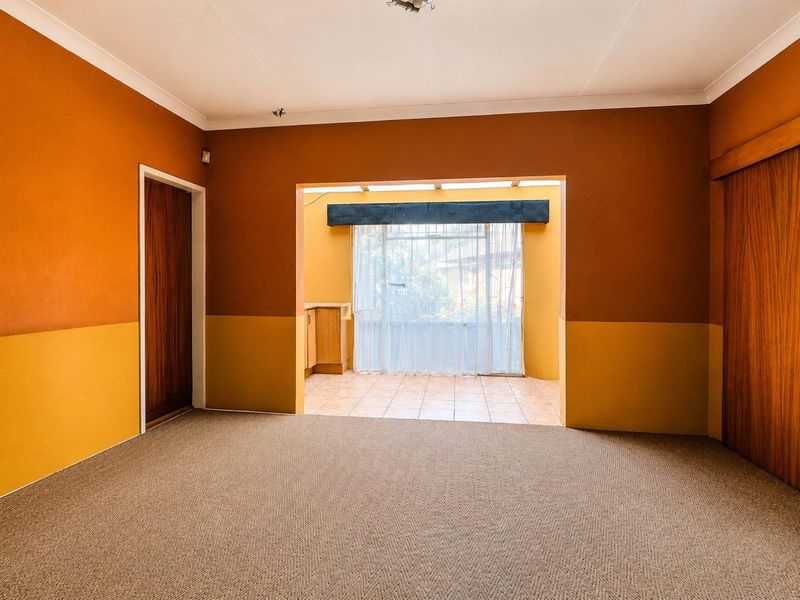 Spacious living area featuring carpeted flooring, built-in cupboards, and an open transition to a sunroom with tiled floors and large windows.