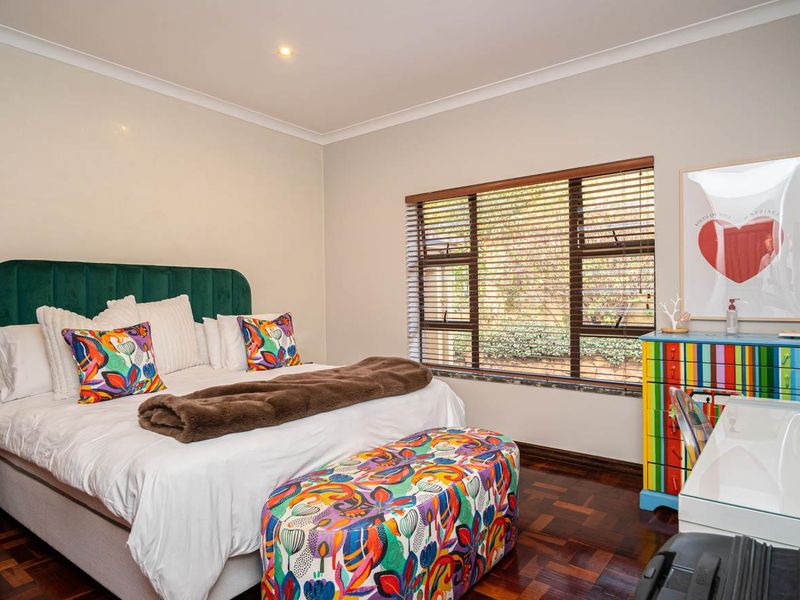 A well-maintained bedroom featuring rich parquet flooring, neutral walls, cove cornicing, and large windows fitted with venetian blinds.