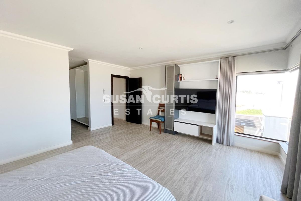 Spacious bedroom featuring light-toned wood-look flooring, built-in cabinetry, and a large window with neutral curtains.