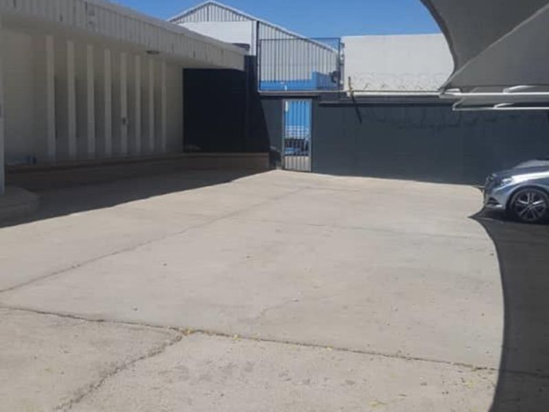 Exterior view of an office property featuring a concrete parking area, shade sail structure, and secure perimeter fencing with razor wire.