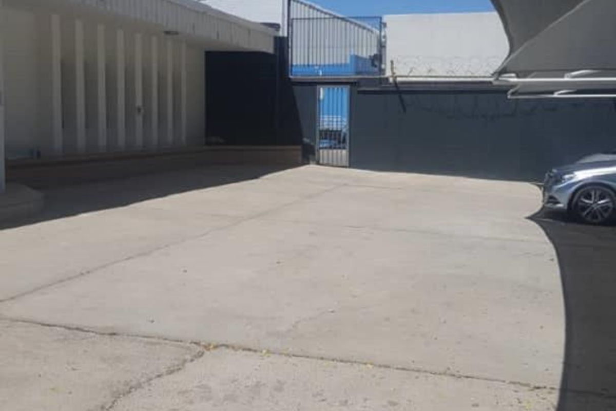 Exterior view of an office property featuring a concrete parking area, shade sail structure, and secure perimeter fencing with razor wire.