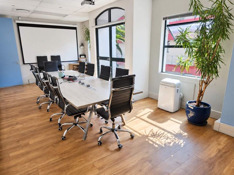 A professional office meeting room featuring laminate flooring, a built-in projector screen, and large windows providing natural light.
