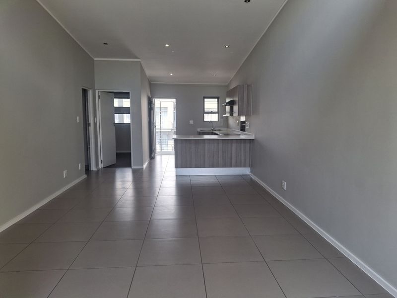 An open-plan living and kitchen area featuring neutral tiled flooring, modern cabinetry, and a breakfast bar, offering a clean and versatile living space.