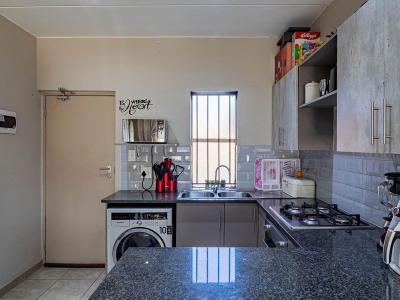 Functional kitchen featuring granite countertops, subway tile backsplash, built-in gas hob, oven, and ample cabinetry with integrated laundry plumbing.