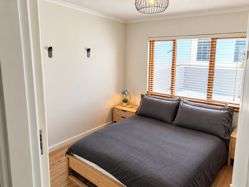 A well-maintained bedroom featuring light laminate flooring, neutral walls, and venetian blinds, offering a clean and comfortable living space.