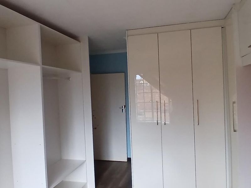 A clean bedroom featuring ample built-in cupboard storage, laminate flooring, and a neutral interior finish, ready for personalization.