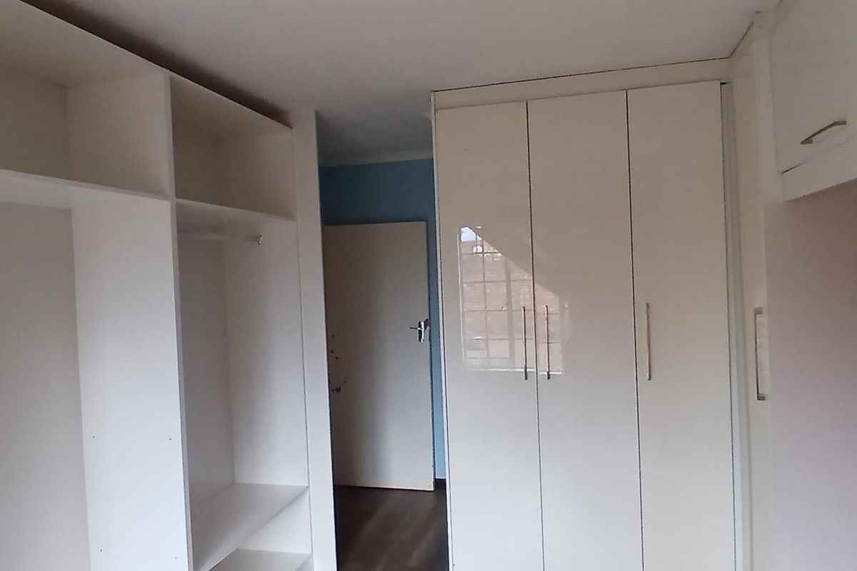A clean bedroom featuring ample built-in cupboard storage, laminate flooring, and a neutral interior finish, ready for personalization.