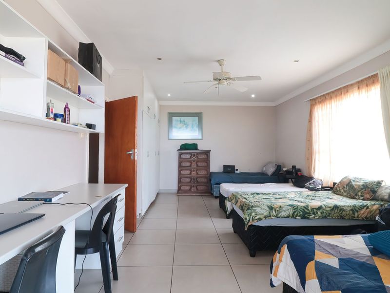 Spacious bedroom featuring tiled flooring, built-in cupboards, a built-in desk with shelving, and a ceiling fan.