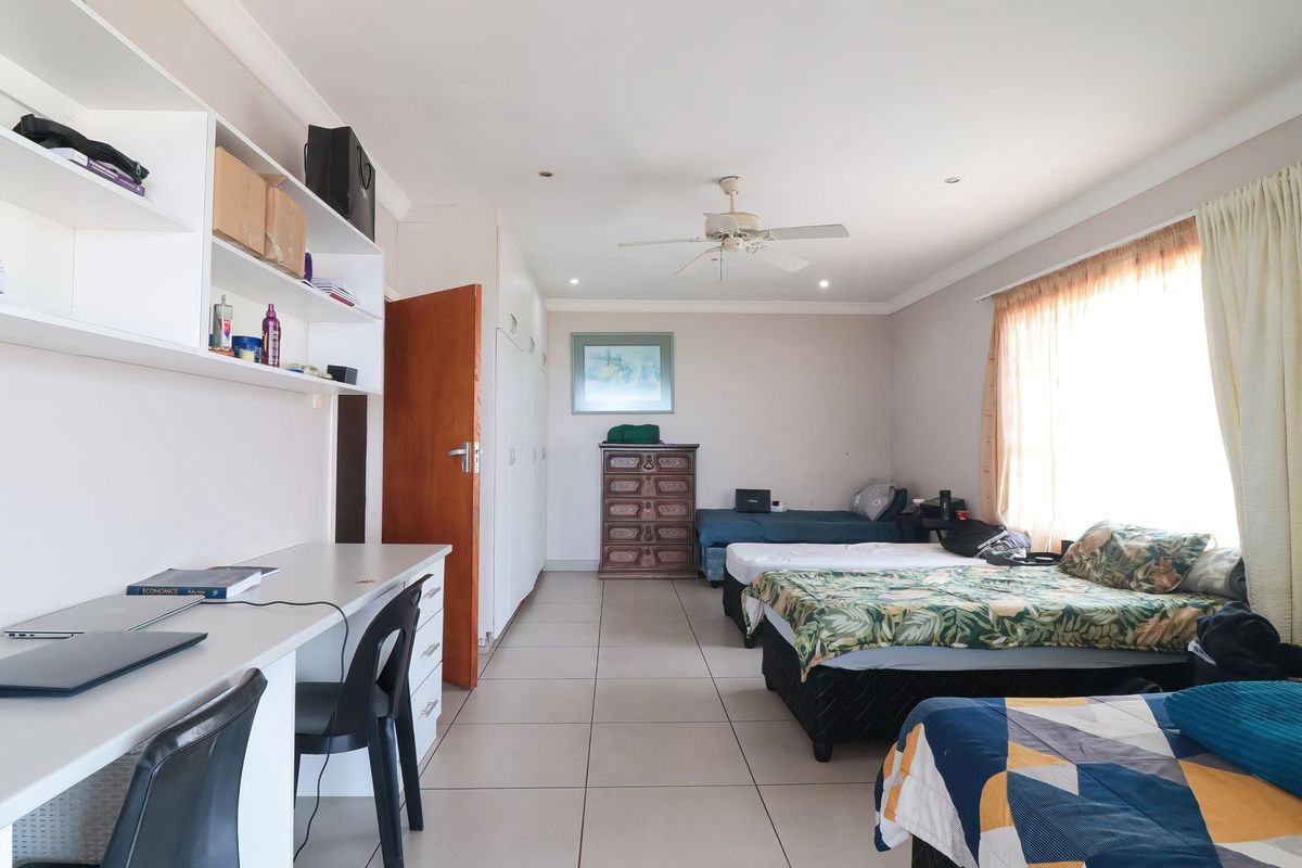Spacious bedroom featuring tiled flooring, built-in cupboards, a built-in desk with shelving, and a ceiling fan.
