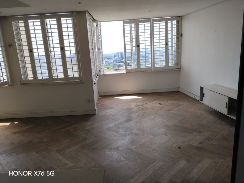 Bright and spacious living area featuring elegant herringbone timber flooring, plantation shutters, and expansive city views, offering a clean canvas for personalization.