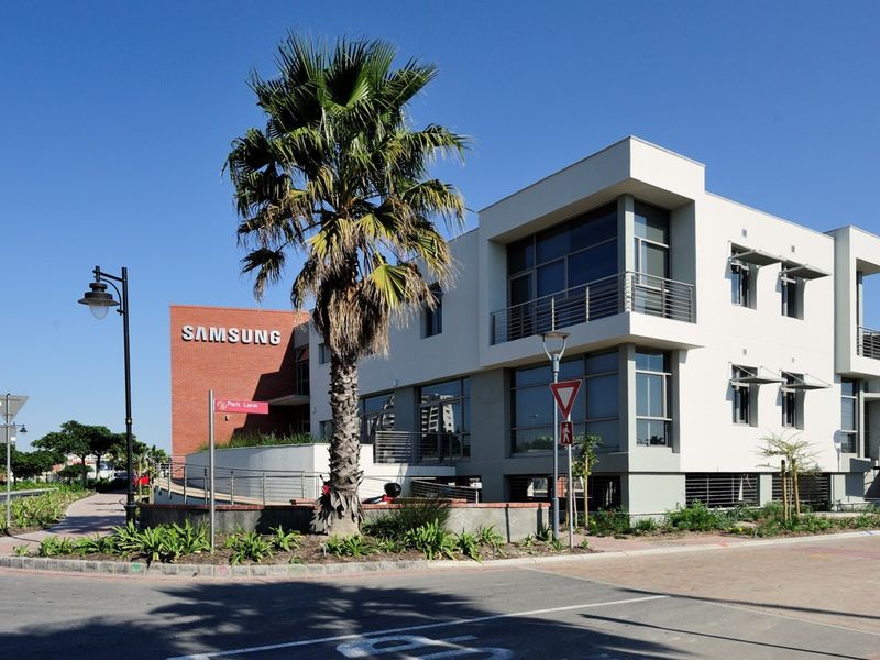 Modern multi-story office building featuring a combination of brick and contemporary white facade, large glass windows, and a balcony, situated on a corner lot.