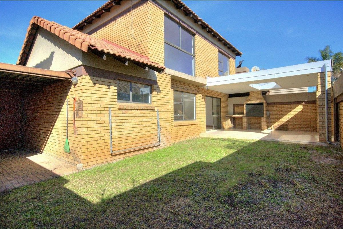 Rear view of a double-story face-brick cluster home featuring a covered patio with a built-in braai and a private garden area.
