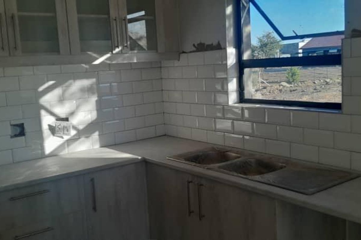 An unfinished kitchen area featuring light wood-look cabinetry, a double basin sink, and a white subway tile backsplash, awaiting final wall finishing and electrical installation.