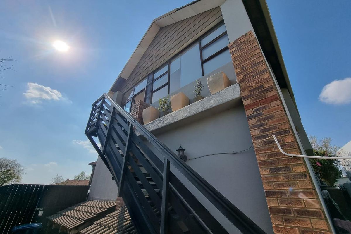 Rear exterior view of the apartment building featuring a prominent external staircase, brick detailing, and large windows providing natural light to the upper level.