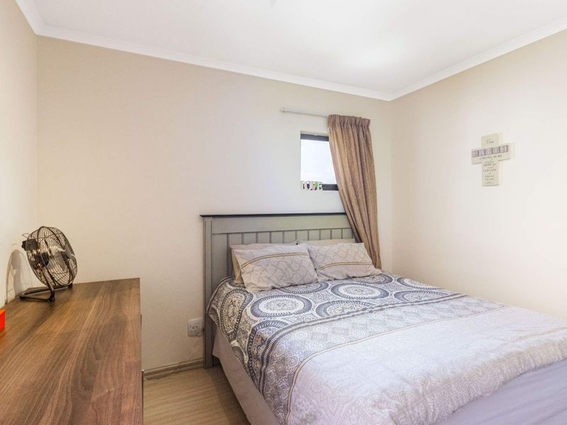 A compact bedroom featuring neutral wall tones, laminate flooring, and a small window, providing a functional and cozy sleeping space.