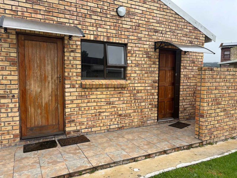 A rear exterior view of a face brick cottage featuring a tiled patio area with two timber entrance doors and protective awnings.