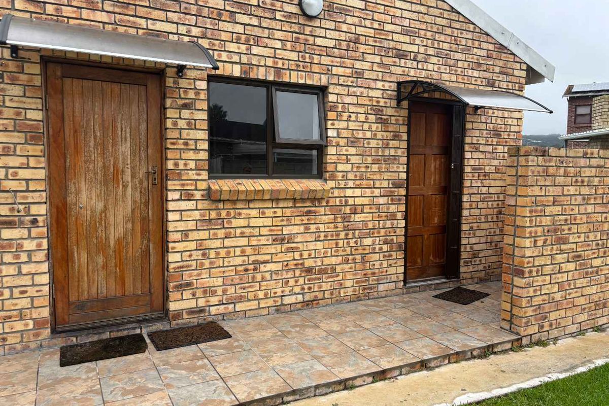 A rear exterior view of a face brick cottage featuring a tiled patio area with two timber entrance doors and protective awnings.