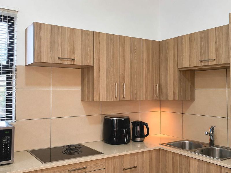 Modern kitchen featuring light wood-grain cabinetry, stone countertops, a stainless steel double sink, and a built-in ceramic hob with tiled splashback.