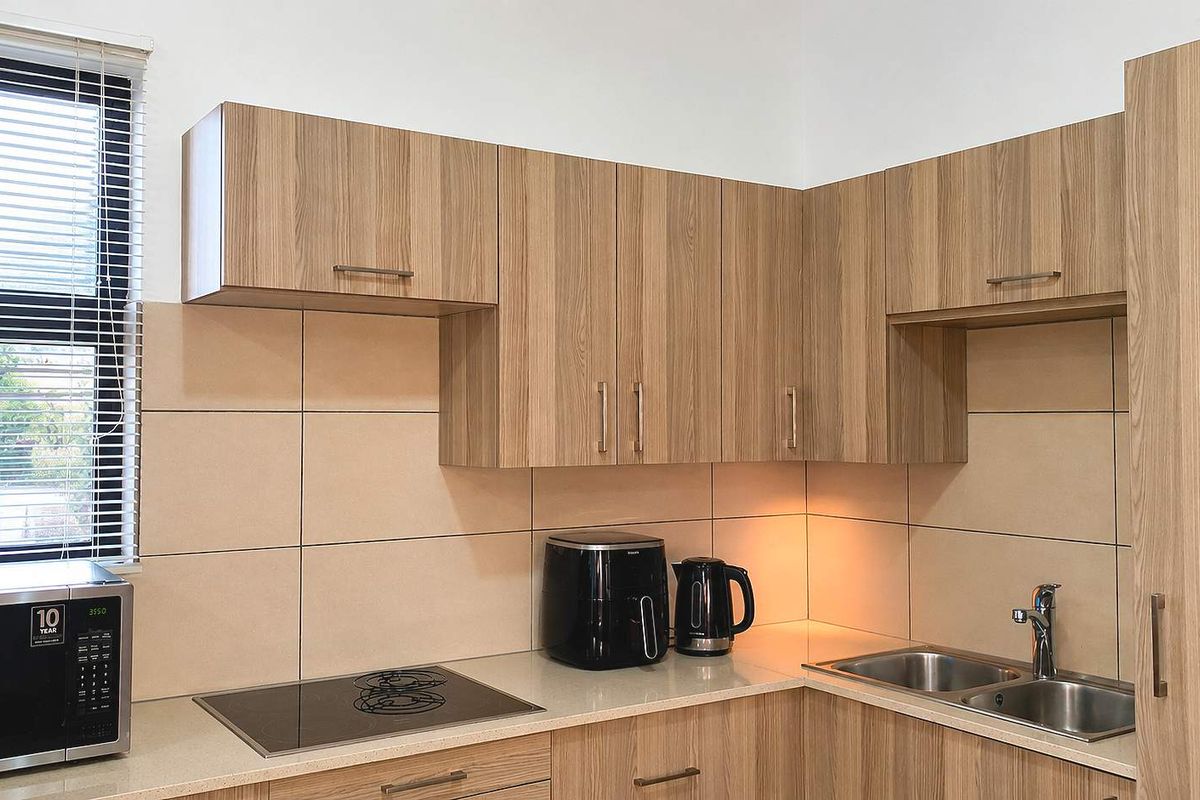 Modern kitchen featuring light wood-grain cabinetry, stone countertops, a stainless steel double sink, and a built-in ceramic hob with tiled splashback.